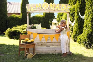 Photo of Little girl pouring natural lemonade into paper cup in park