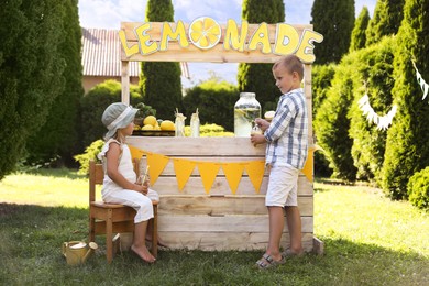 Little girl sitting on chair while boy pouring lemonade into paper cup in park