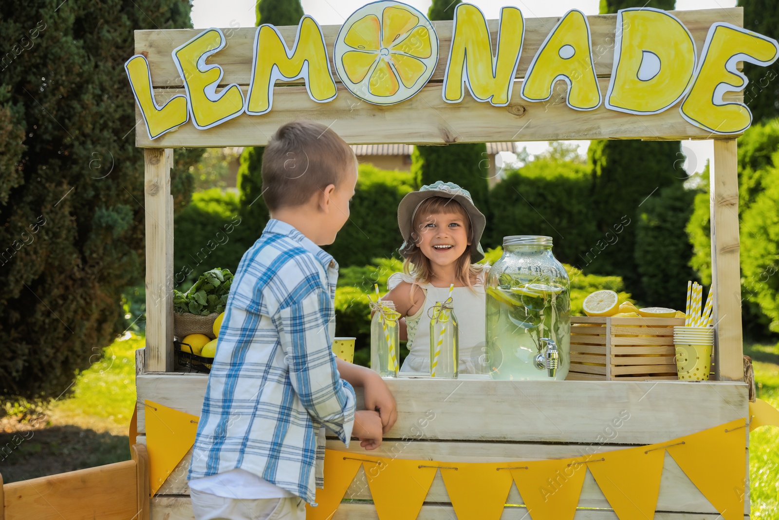 Photo of Cute little girl selling natural lemonade to boy in park