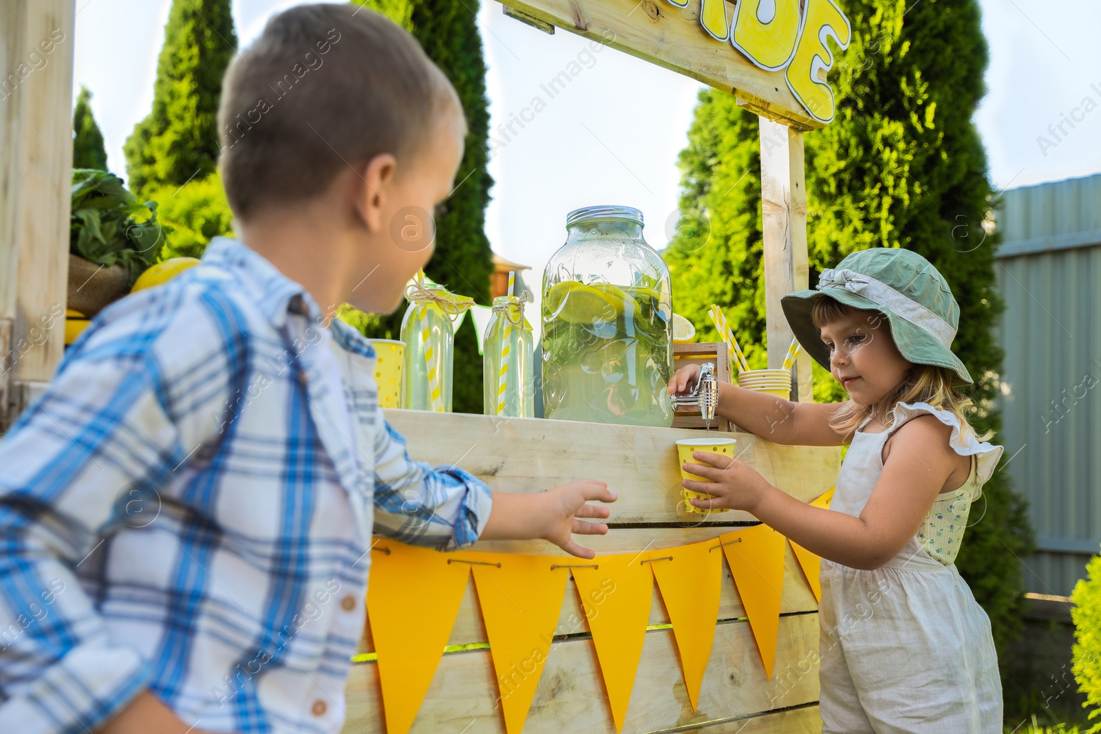 Photo of Cute little girl pouring natural lemonade into cup for boy in park