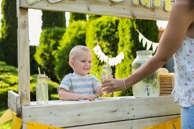 Cute little boy selling natural lemonade to woman in park