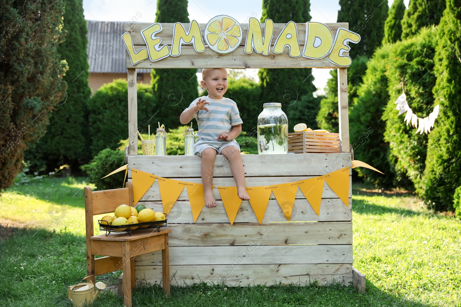 Photo of Cute little boy sitting on lemonade stand in park