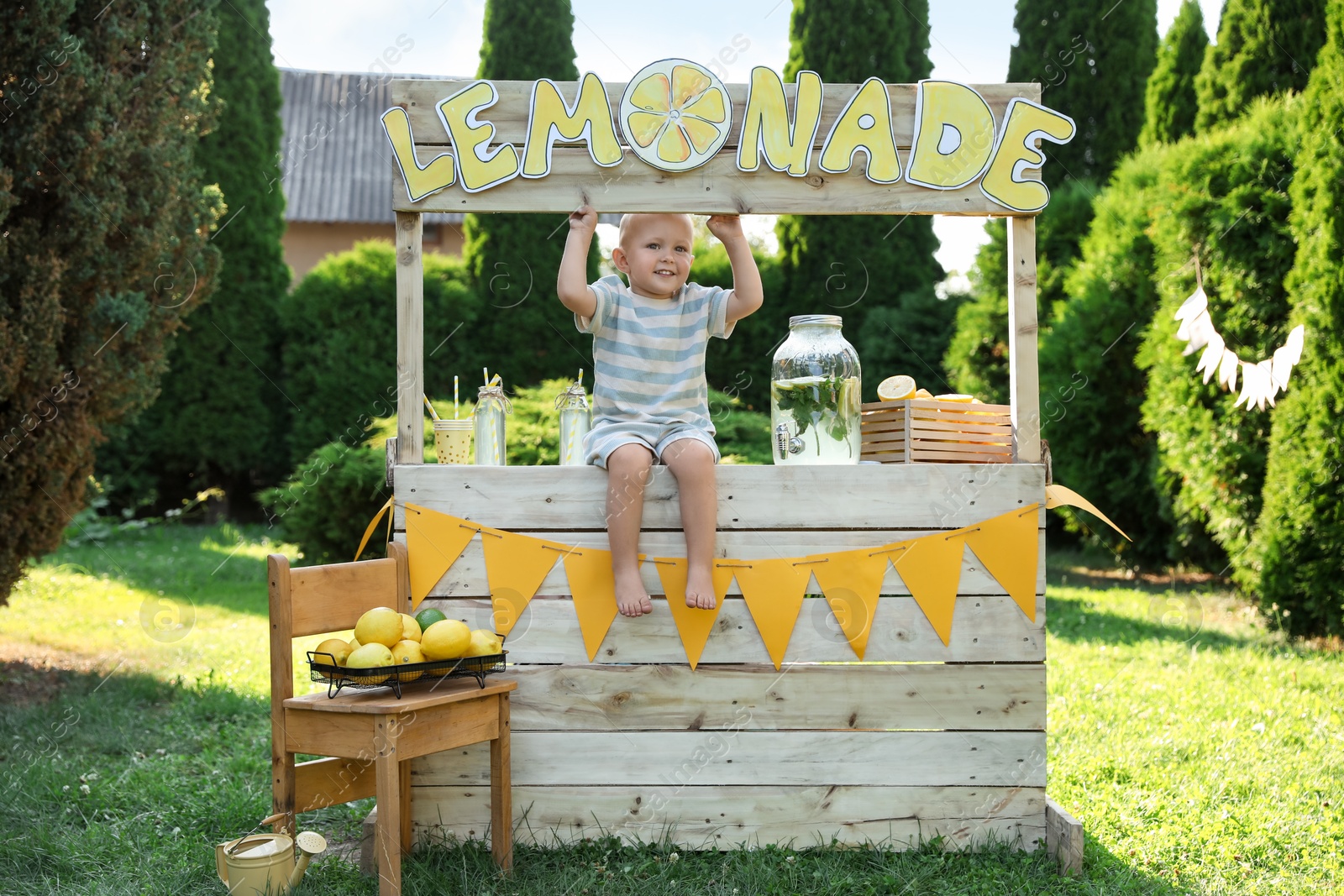 Photo of Cute little boy sitting on lemonade stand in park