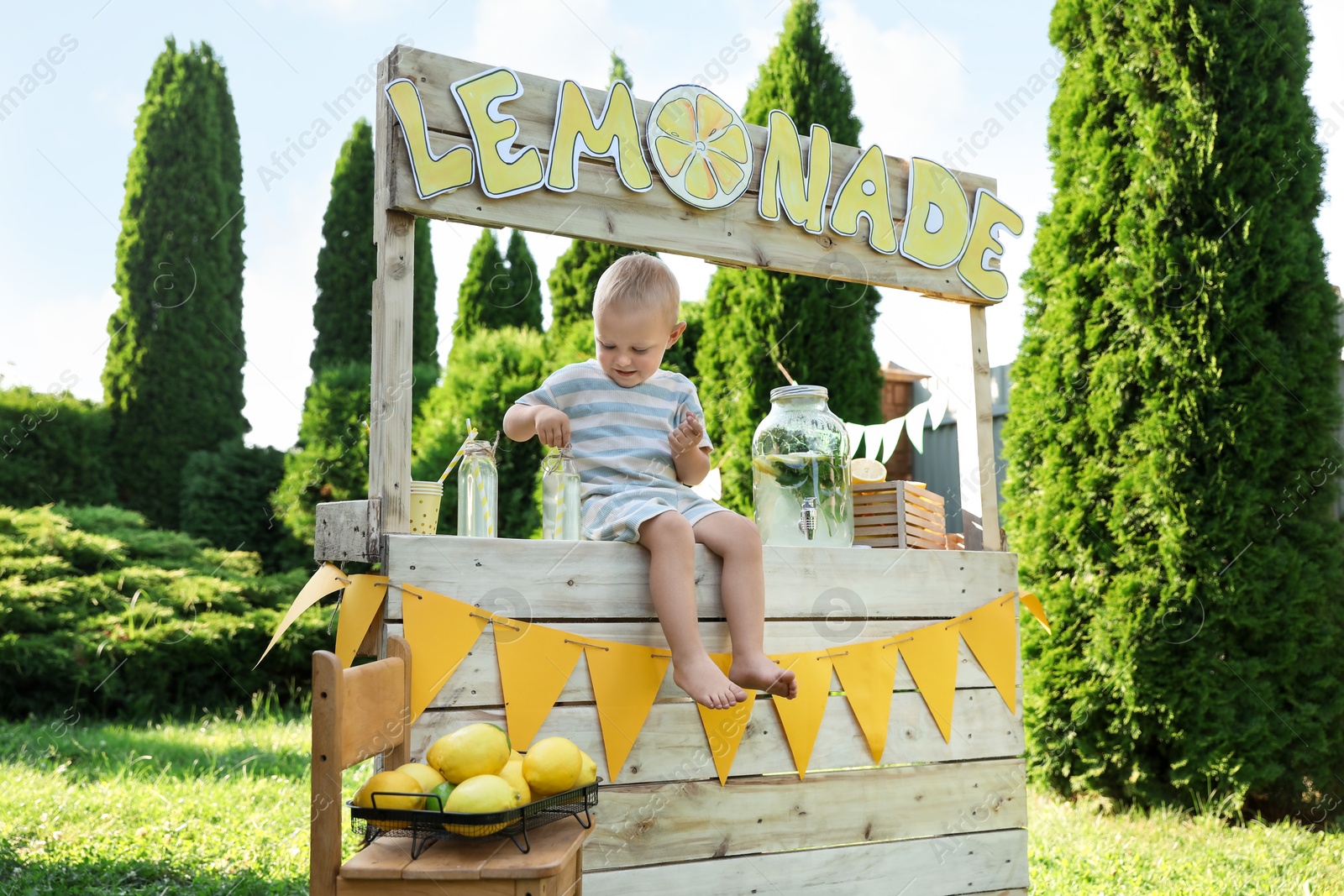 Photo of Cute little boy sitting on lemonade stand in park