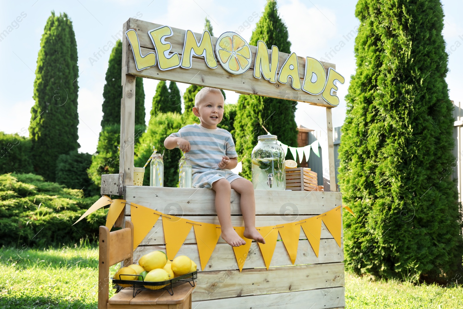 Photo of Cute little boy sitting on lemonade stand in park