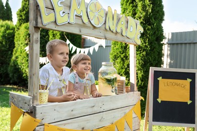 Photo of Cute little kids with refreshing drinks at lemonade stand in park