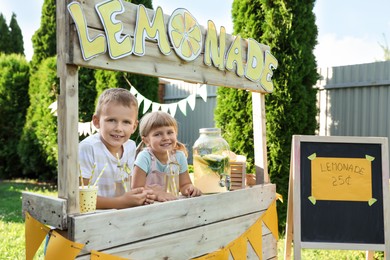 Photo of Cute little kids with refreshing drinks at lemonade stand in park