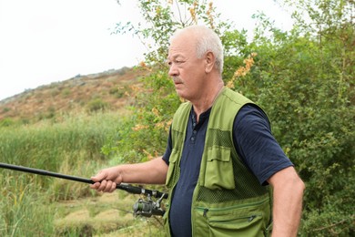 Fisherman with rod fishing near lake at summer