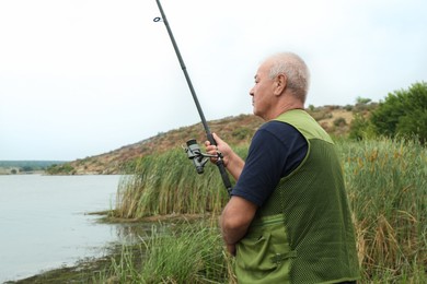 Fisherman with rod fishing near lake at summer