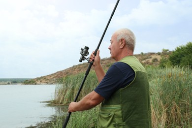 Fisherman with rod fishing near lake at summer