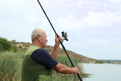 Fisherman with rod fishing near lake at summer