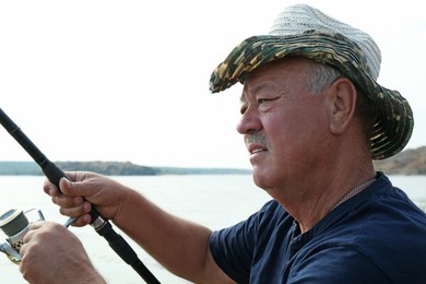 Fisherman with rod fishing near lake at summer