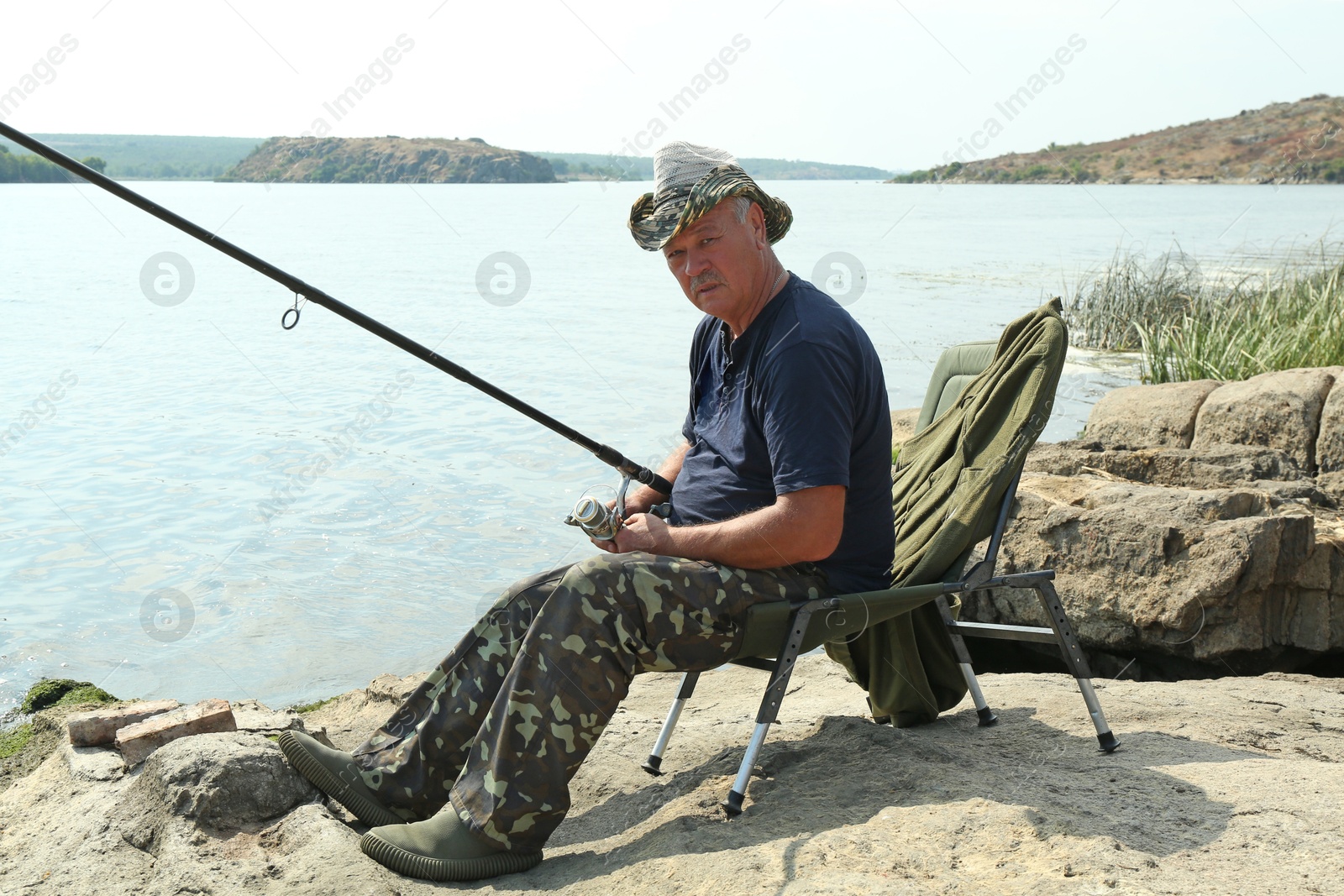 Photo of Fisherman with rod sitting on chair and fishing near lake at summer