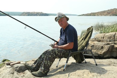 Fisherman with rod sitting on chair and fishing near lake at summer