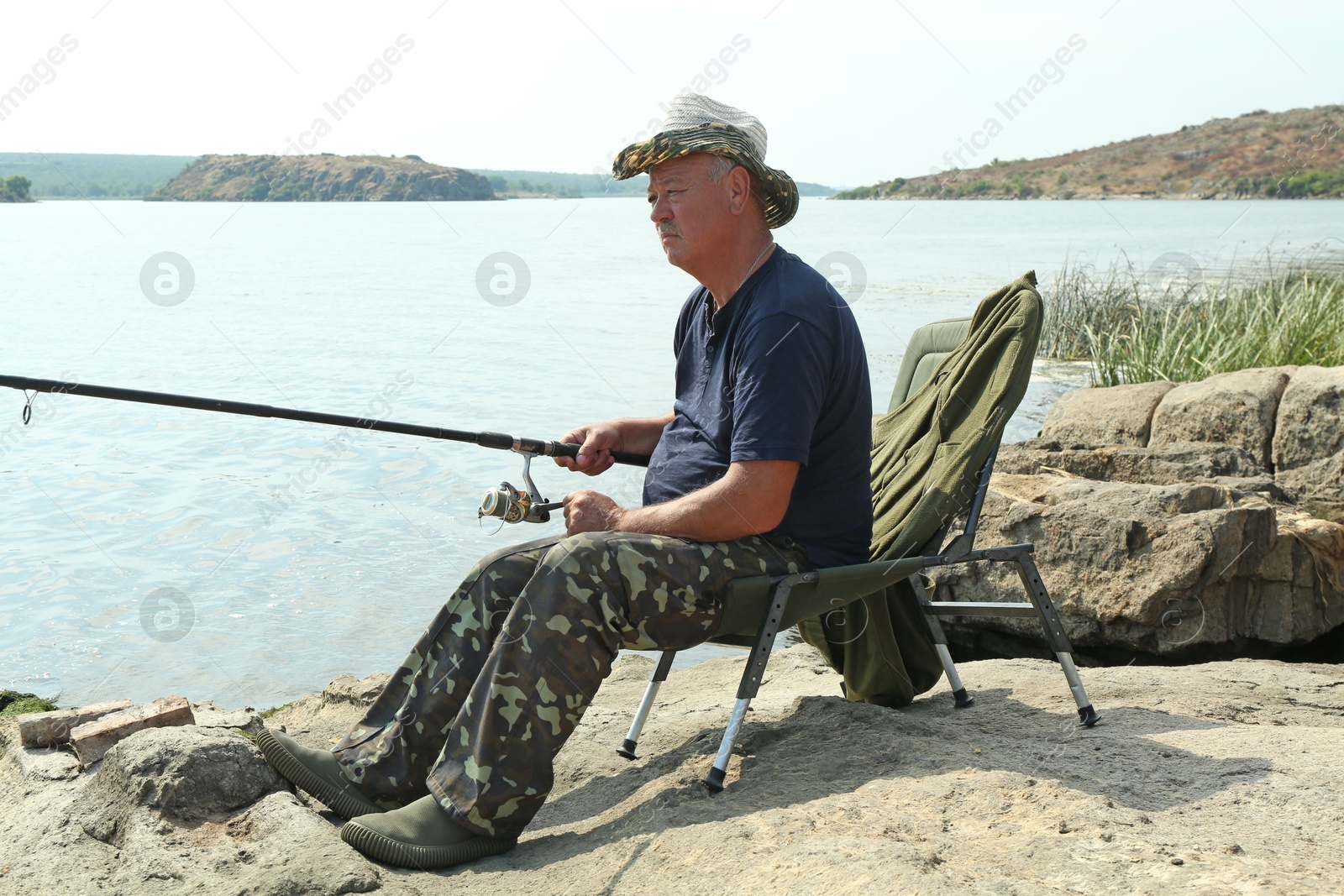 Photo of Fisherman with rod sitting on chair and fishing near lake at summer