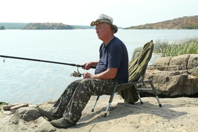 Fisherman with rod sitting on chair and fishing near lake at summer