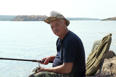 Photo of Fisherman with rod sitting on chair and fishing near lake at summer