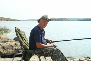 Photo of Fisherman with rod sitting on chair and fishing near lake at summer