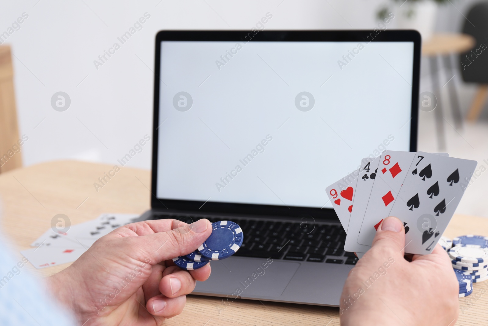 Photo of Online poker. Man with playing cards, chips and laptop at wooden table indoors, closeup