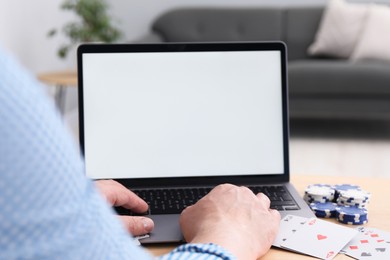 Photo of Online poker. Man with playing cards and chips using laptop at wooden table indoors, closeup