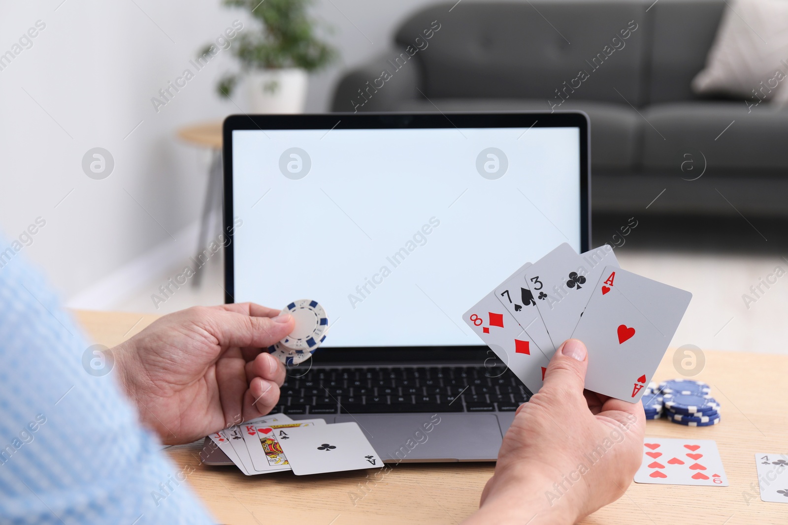 Photo of Online poker. Man with playing cards, chips and laptop at wooden table indoors, closeup