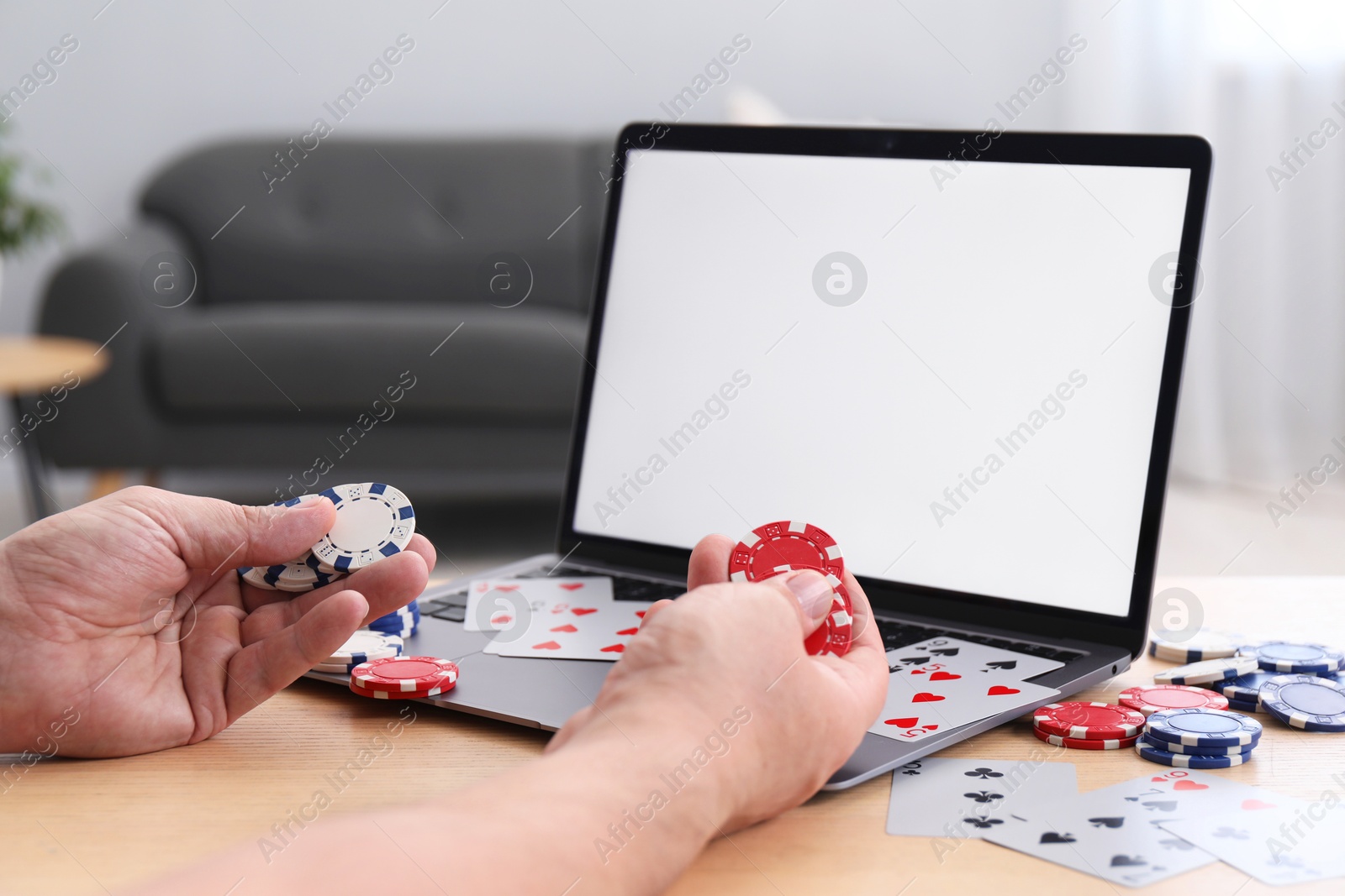 Photo of Online poker. Man with playing cards, chips and laptop at wooden table indoors, closeup