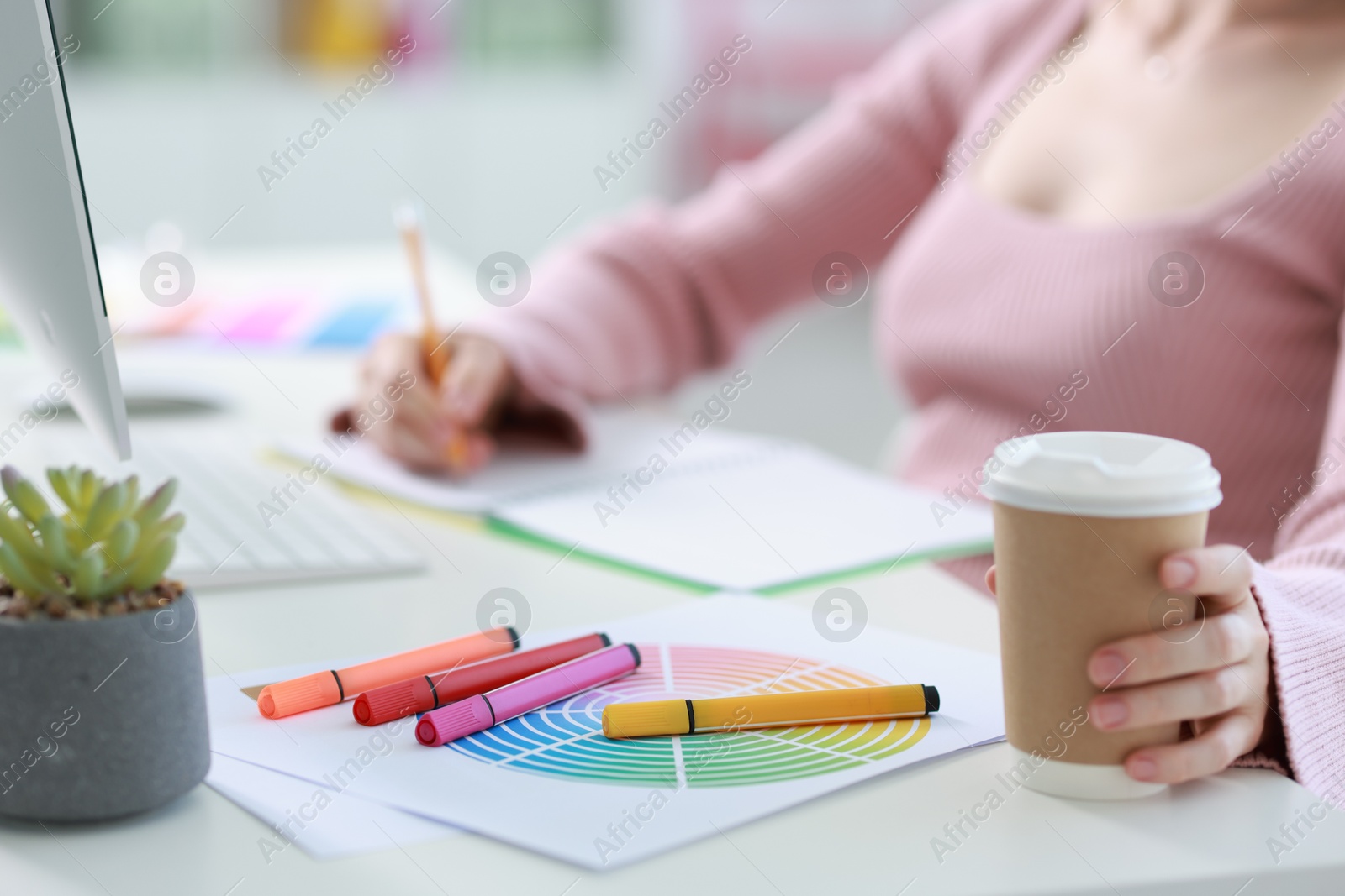 Photo of Designer with paper cup of drink working at table in office, closeup