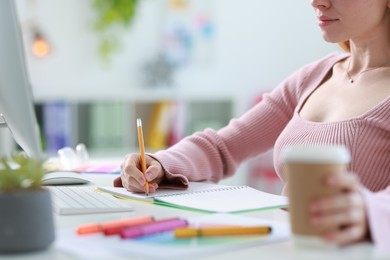 Designer with paper cup of drink working at table in office, closeup