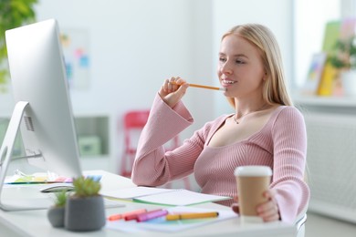 Designer with paper cup of drink working at table in office