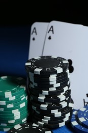 Photo of Playing cards and poker chips on blue table against dark background, closeup