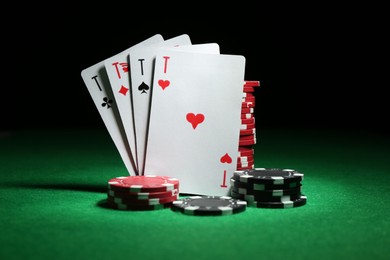 Photo of Playing cards and poker chips on green table against dark background