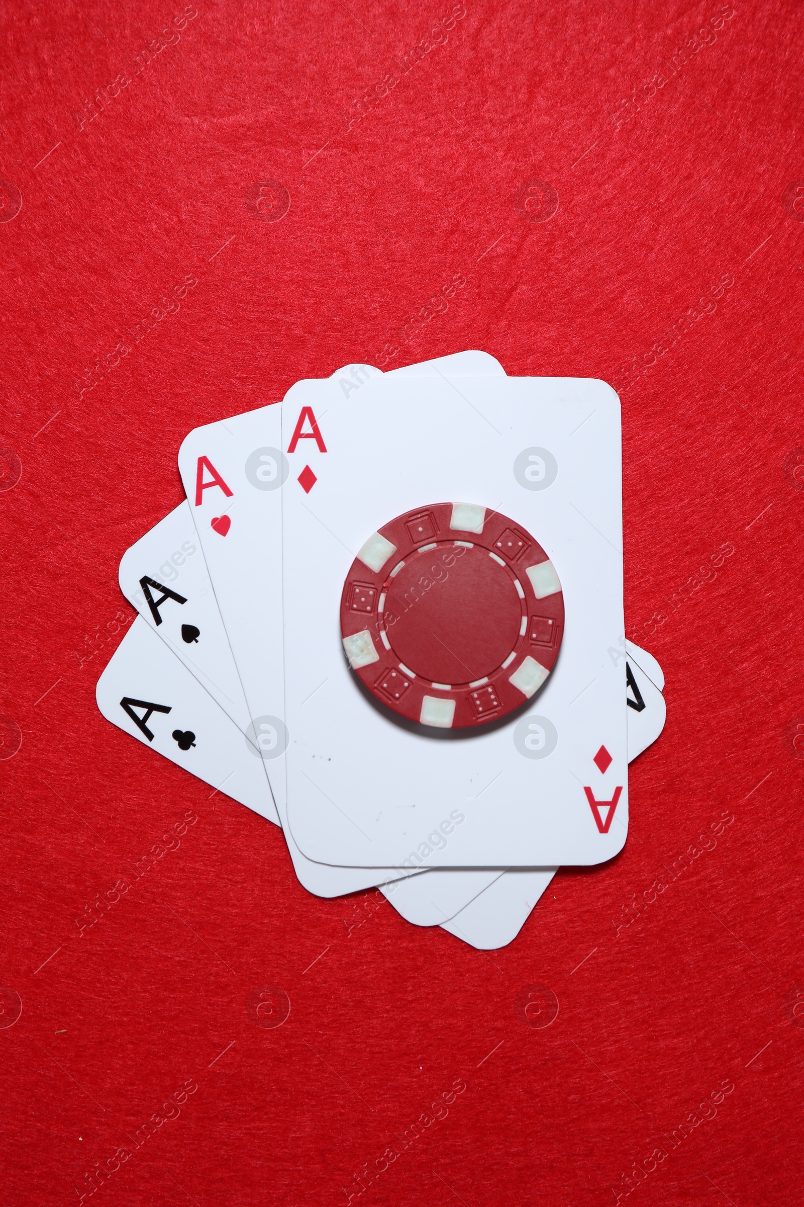 Photo of Playing cards and poker chip on red table, top view