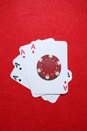 Playing cards and poker chip on red table, top view