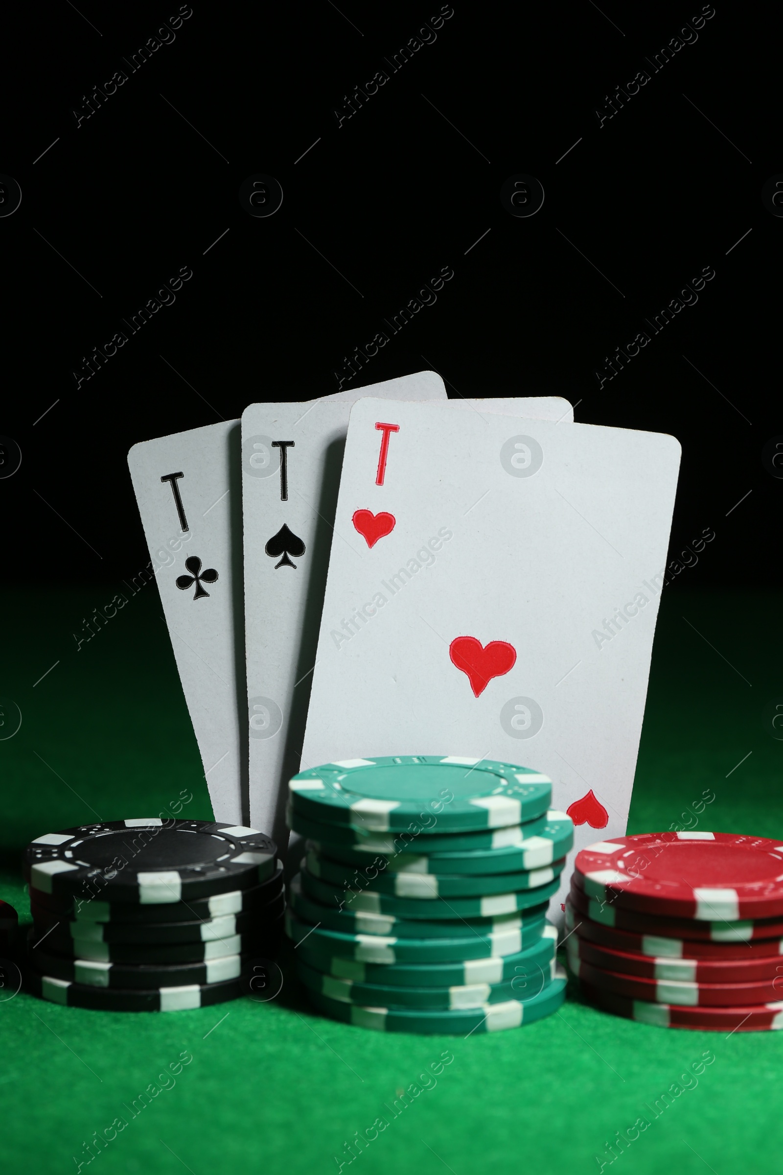 Photo of Playing cards and poker chips on green table against dark background