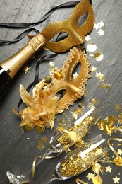 Beautiful golden carnival mask, bottle of sparkling wine, glasses and confetti on gray textured table, flat lay