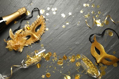 Beautiful golden carnival mask, bottle of sparkling wine, glasses and confetti on gray textured table, flat lay. Space for text