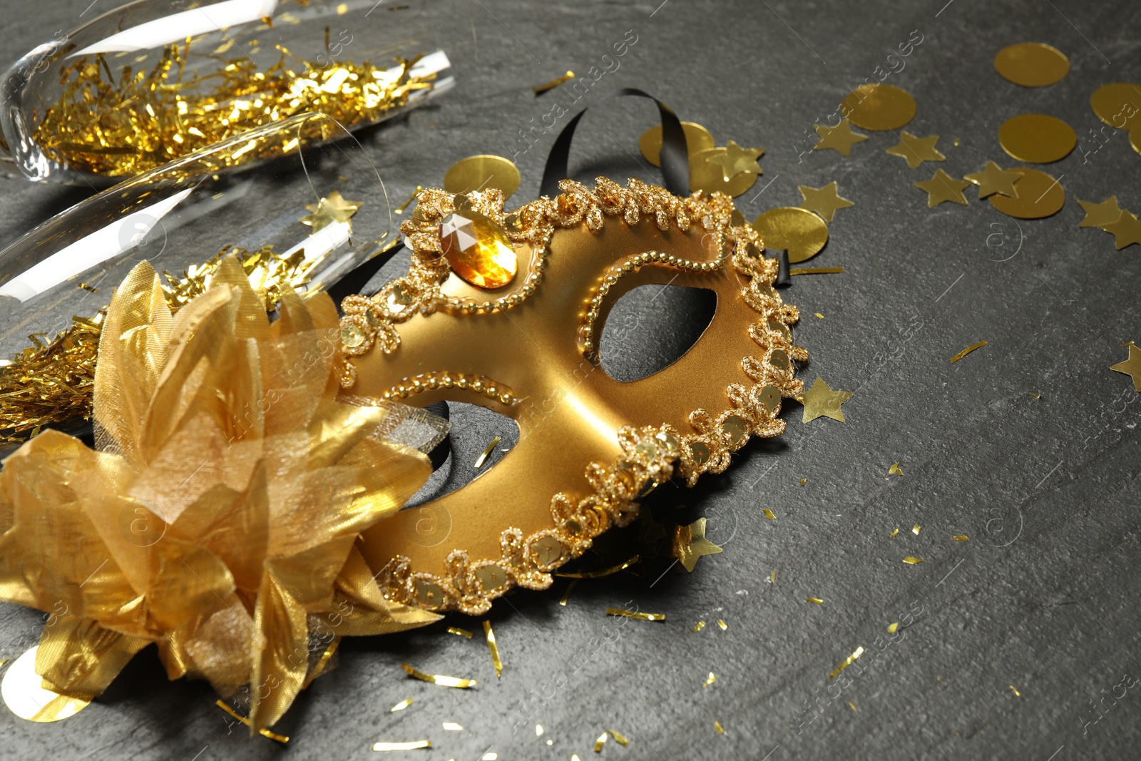 Photo of Beautiful golden carnival mask and glasses on gray textured table, closeup