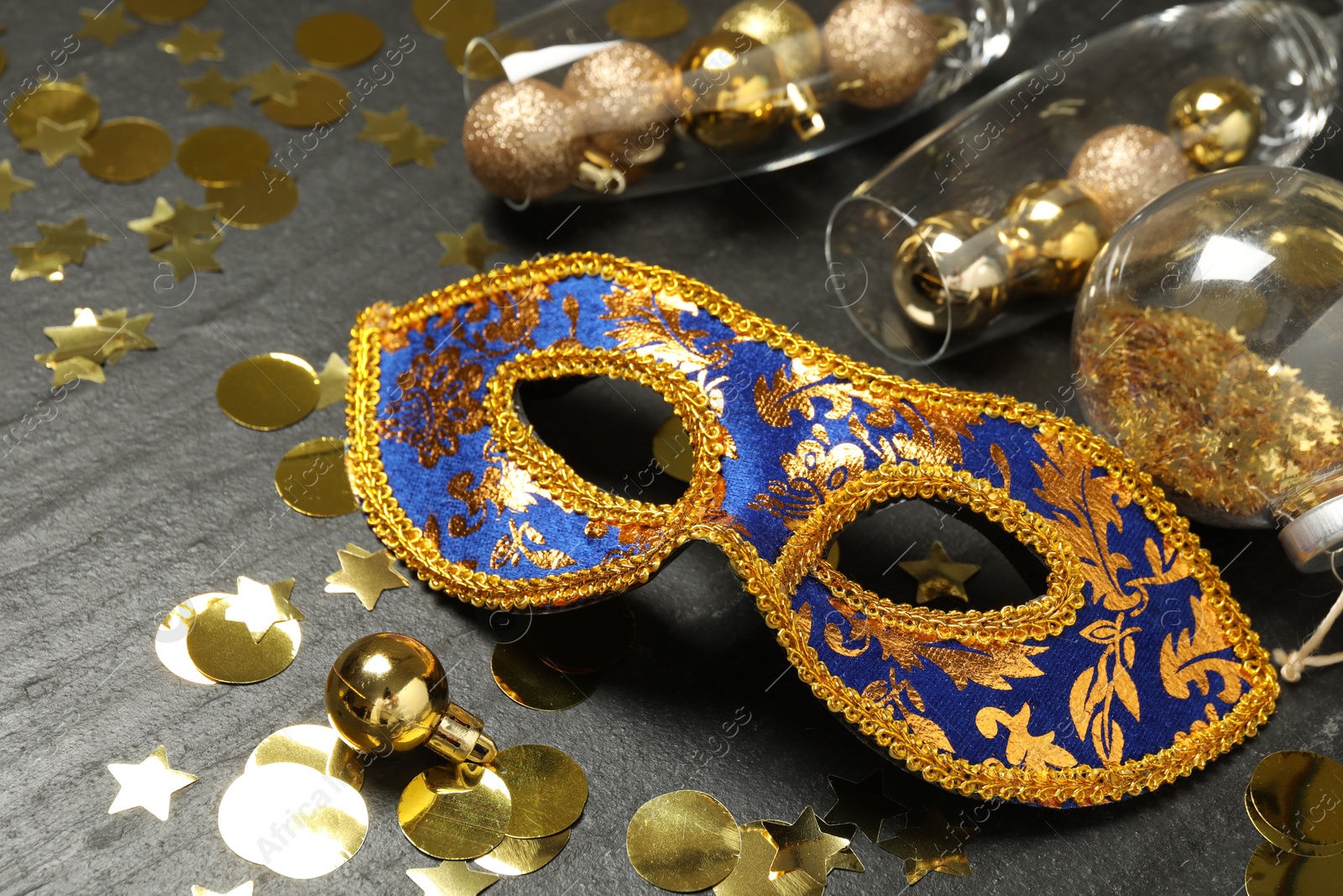 Photo of Beautiful golden carnival mask, glasses with decorative balls and confetti on gray textured table, closeup