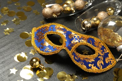 Beautiful golden carnival mask, glasses with decorative balls and confetti on gray textured table, closeup