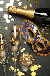 Photo of Beautiful golden carnival mask, bottle of sparkling wine, glasses with decorative balls and confetti on gray textured table, flat lay