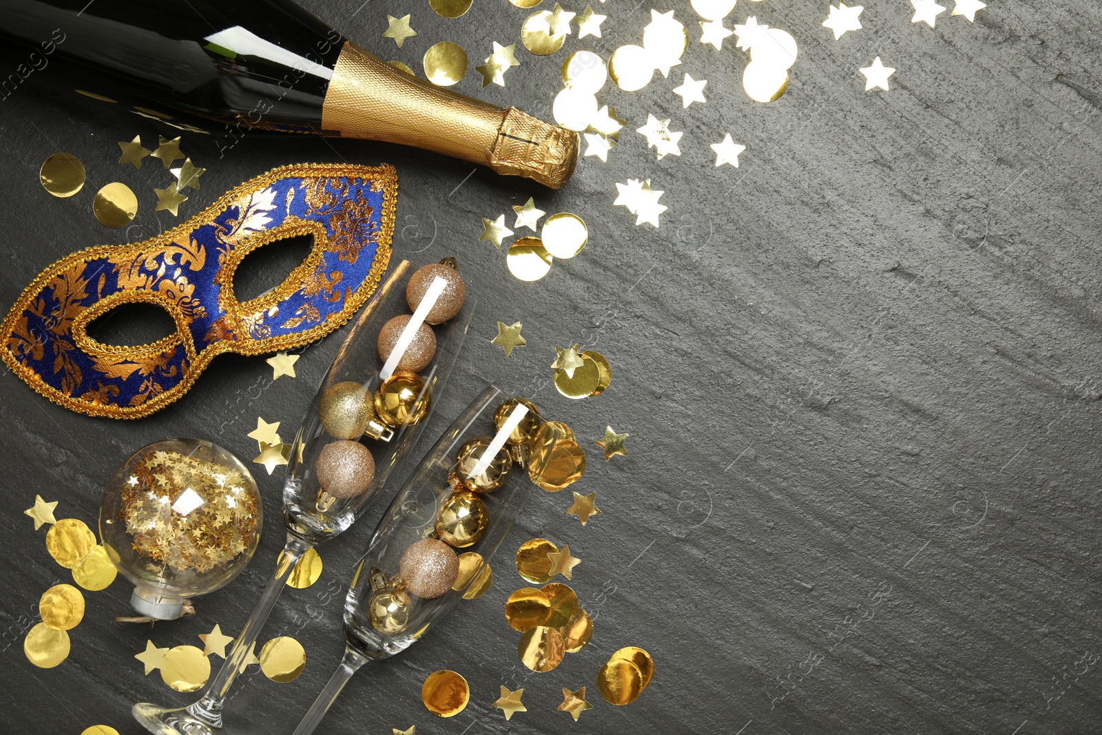 Photo of Beautiful golden carnival mask, bottle of sparkling wine, glasses with decorative balls and confetti on gray textured table, flat lay. Space for text