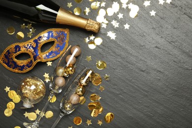 Beautiful golden carnival mask, bottle of sparkling wine, glasses with decorative balls and confetti on gray textured table, flat lay. Space for text