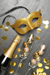 Photo of Beautiful golden carnival mask, bottle of sparkling wine, glasses with decorative balls and confetti on gray textured table, flat lay