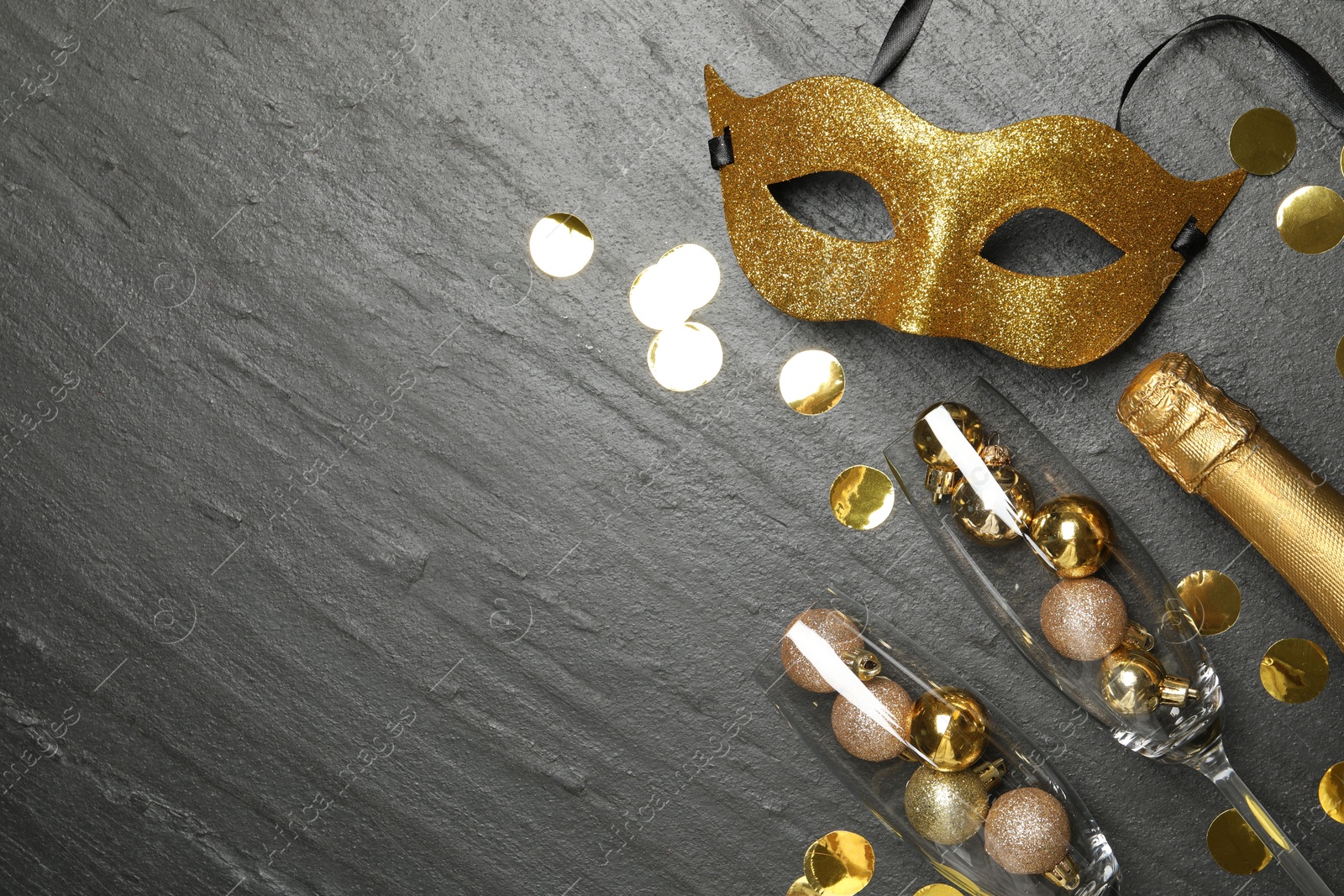 Photo of Beautiful golden carnival mask, bottle of sparkling wine, glasses with decorative balls and confetti on gray textured table, flat lay. Space for text