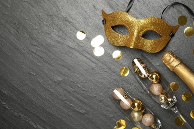 Beautiful golden carnival mask, bottle of sparkling wine, glasses with decorative balls and confetti on gray textured table, flat lay. Space for text