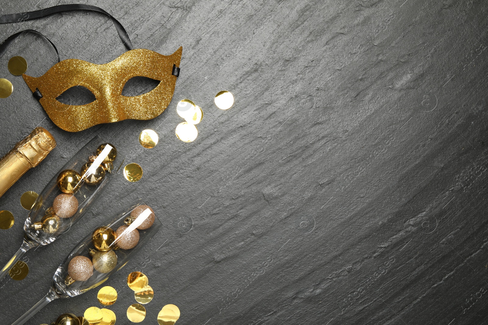 Photo of Beautiful golden carnival mask, bottle of sparkling wine, glasses with decorative balls and confetti on gray textured table, flat lay. Space for text