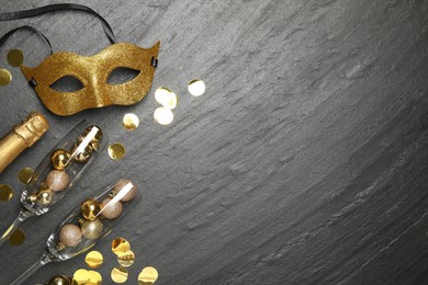 Photo of Beautiful golden carnival mask, bottle of sparkling wine, glasses with decorative balls and confetti on gray textured table, flat lay. Space for text