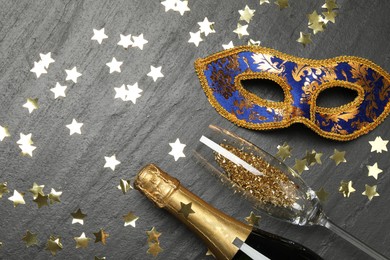 Photo of Beautiful golden carnival mask, bottle of sparkling wine, glass and confetti on gray textured table, flat lay