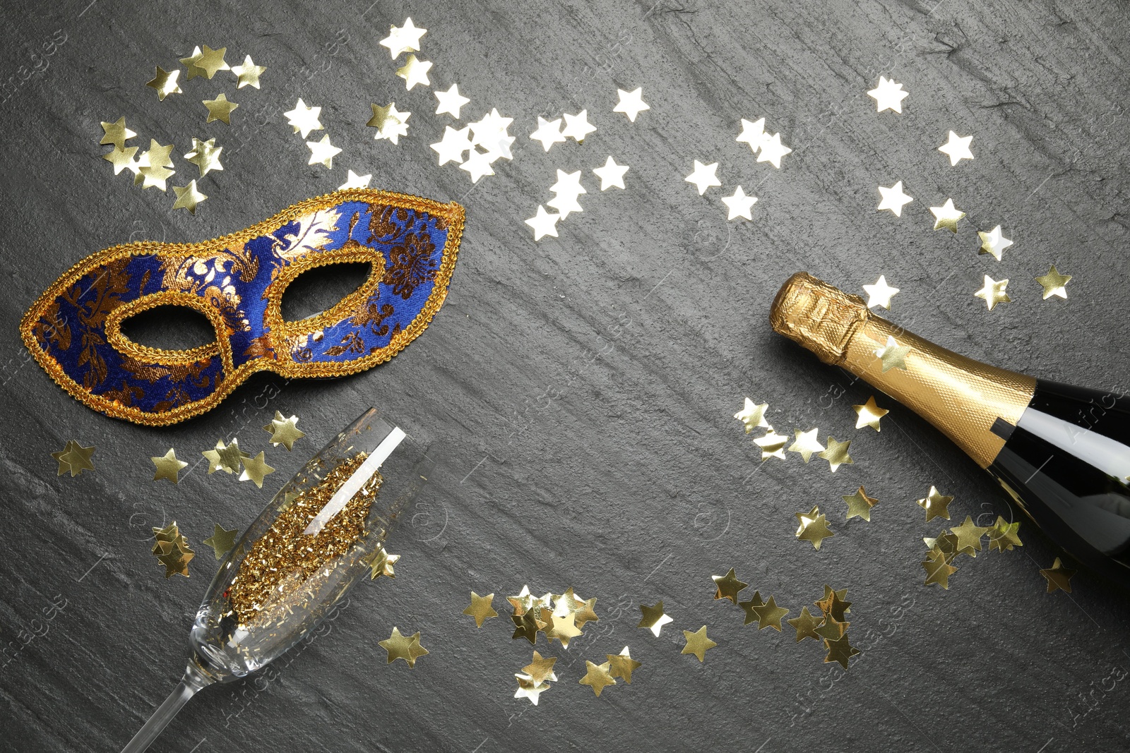 Photo of Beautiful golden carnival mask, bottle of sparkling wine, glass and confetti on gray textured table, flat lay. Space for text