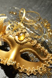 Photo of Beautiful golden carnival mask, glass and confetti on gray textured table, closeup